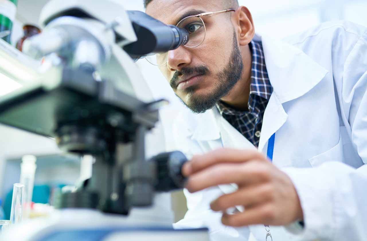 Portrait of young scientist looking in microscope while working on medical research in science laboratory.