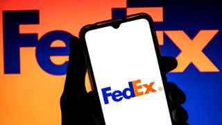 The FedEx logo shown on a phone held by a hand, half-covering a wall bearing the FedEx logo