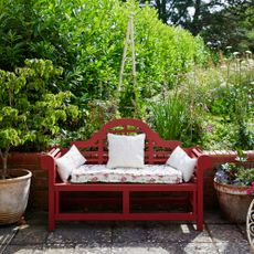 A red-painted curved wooden garden bench in a garden with flower beds and large terracorra plant pots