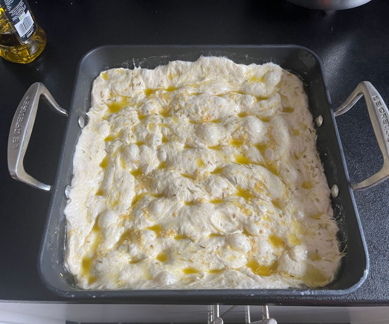 A black square tray of focaccia dough.