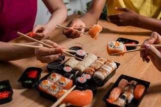 A group of people eating sushi with chopsticks