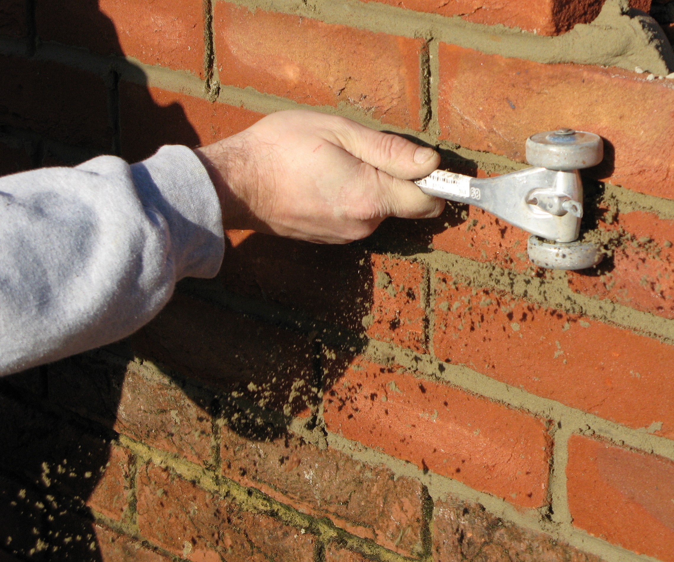 A mortar rake tool removing mortar between bricks