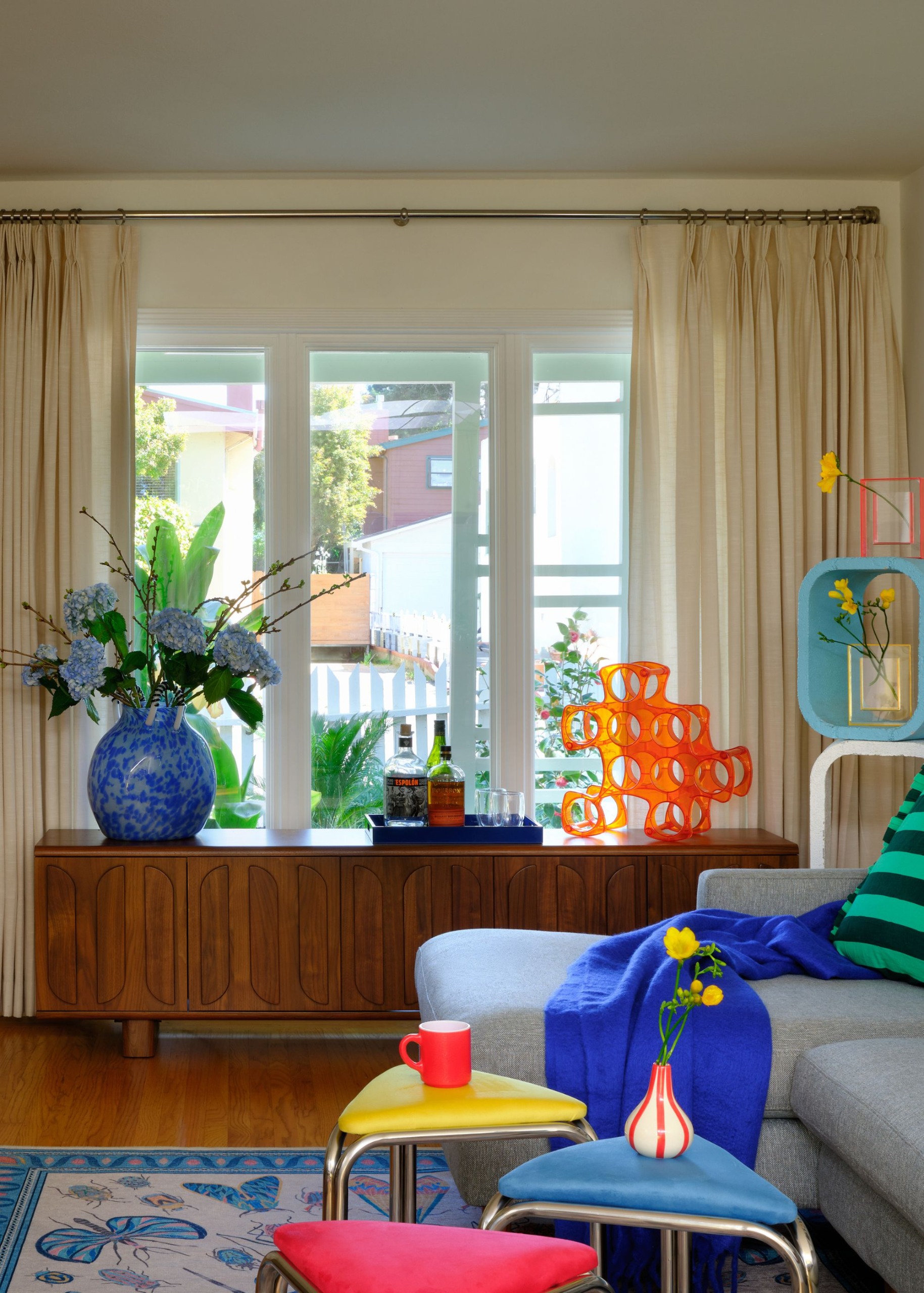A living room with a grey sofa, blue throw, multicolored stools and pop-toned accessories