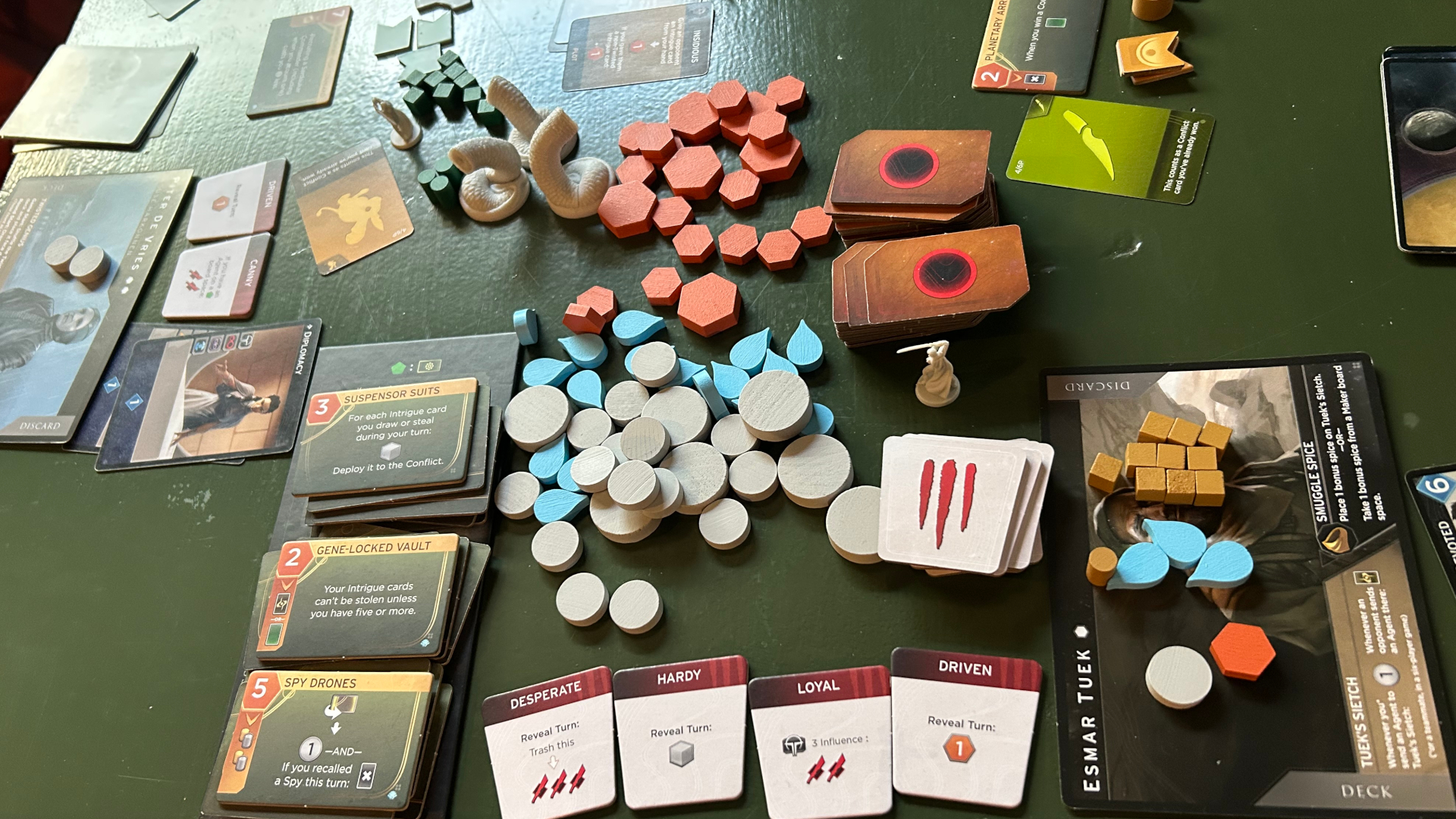 Dune: Imperium - Bloodlines tokens and cards on a green surface, with Uprising Sandworm models added to the mix