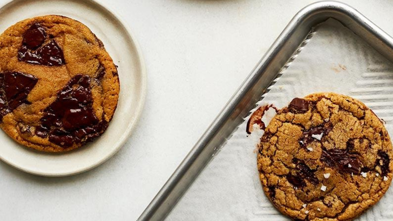 Muscovado dark chocolate chip cookies on a baking tray alongside a plate 