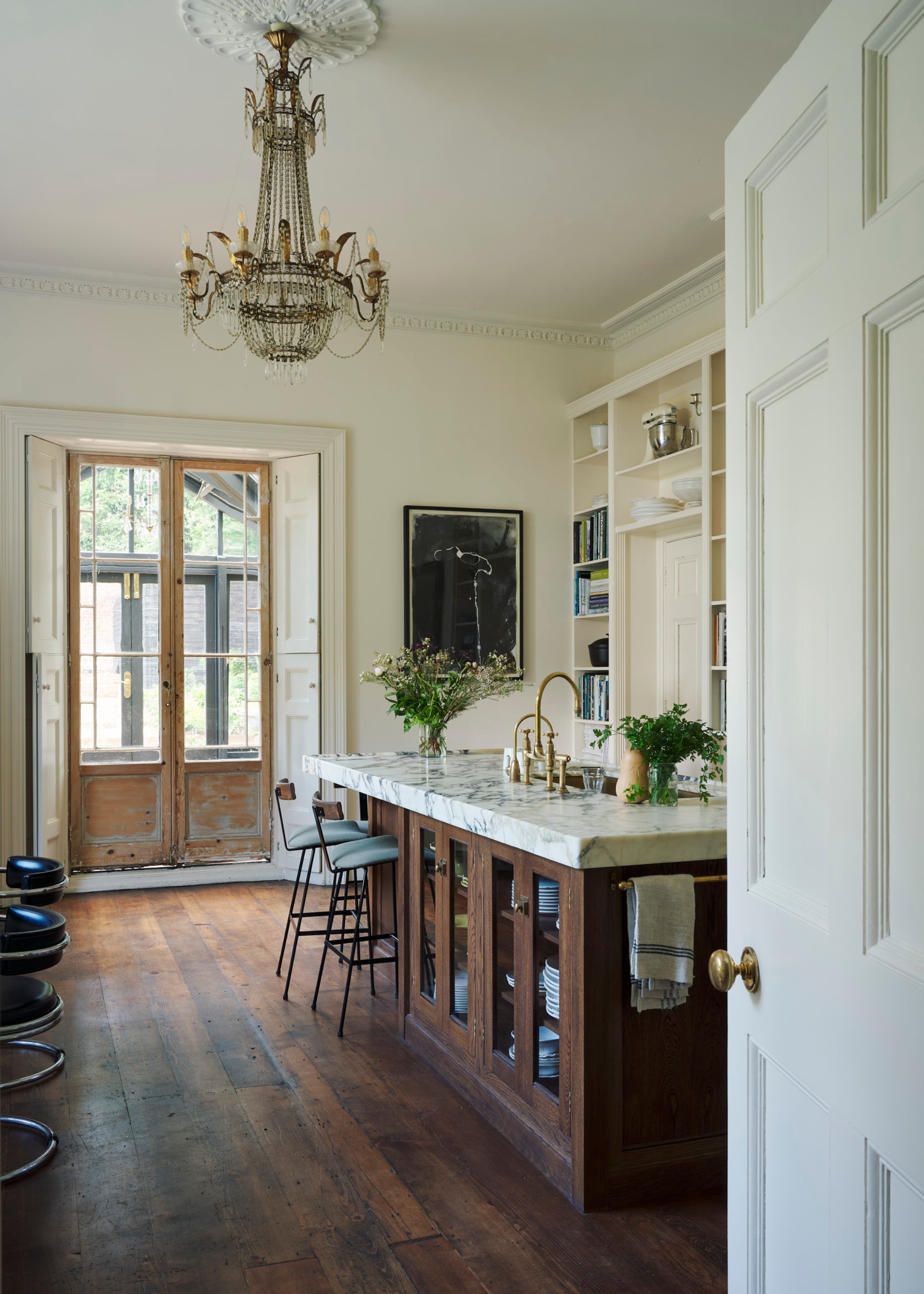 A dark wood kitchen with a central wood island with a light marble worktop, french doors at the side and dark wood flooring