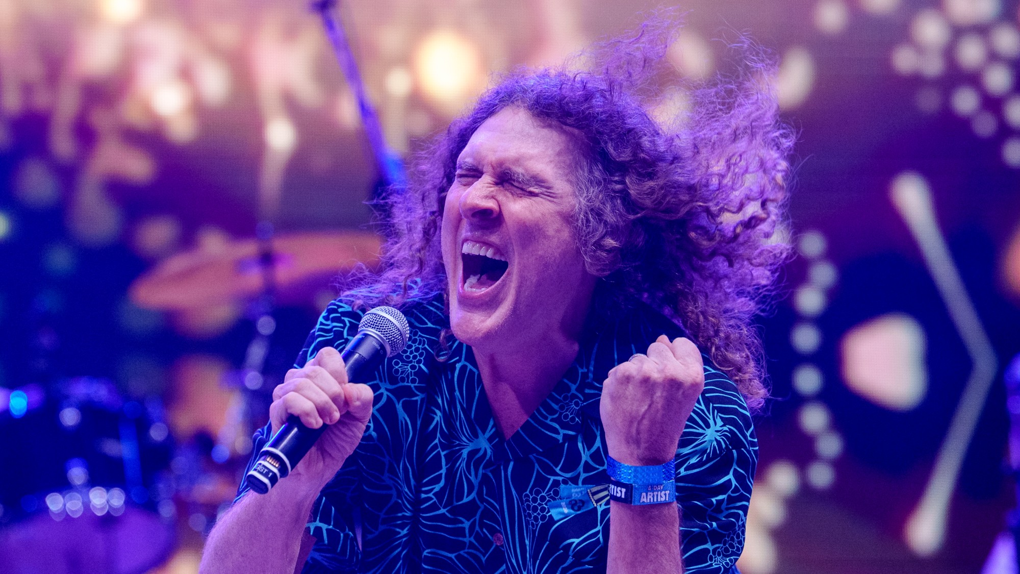 a man with curly, long hair sings into a microphone