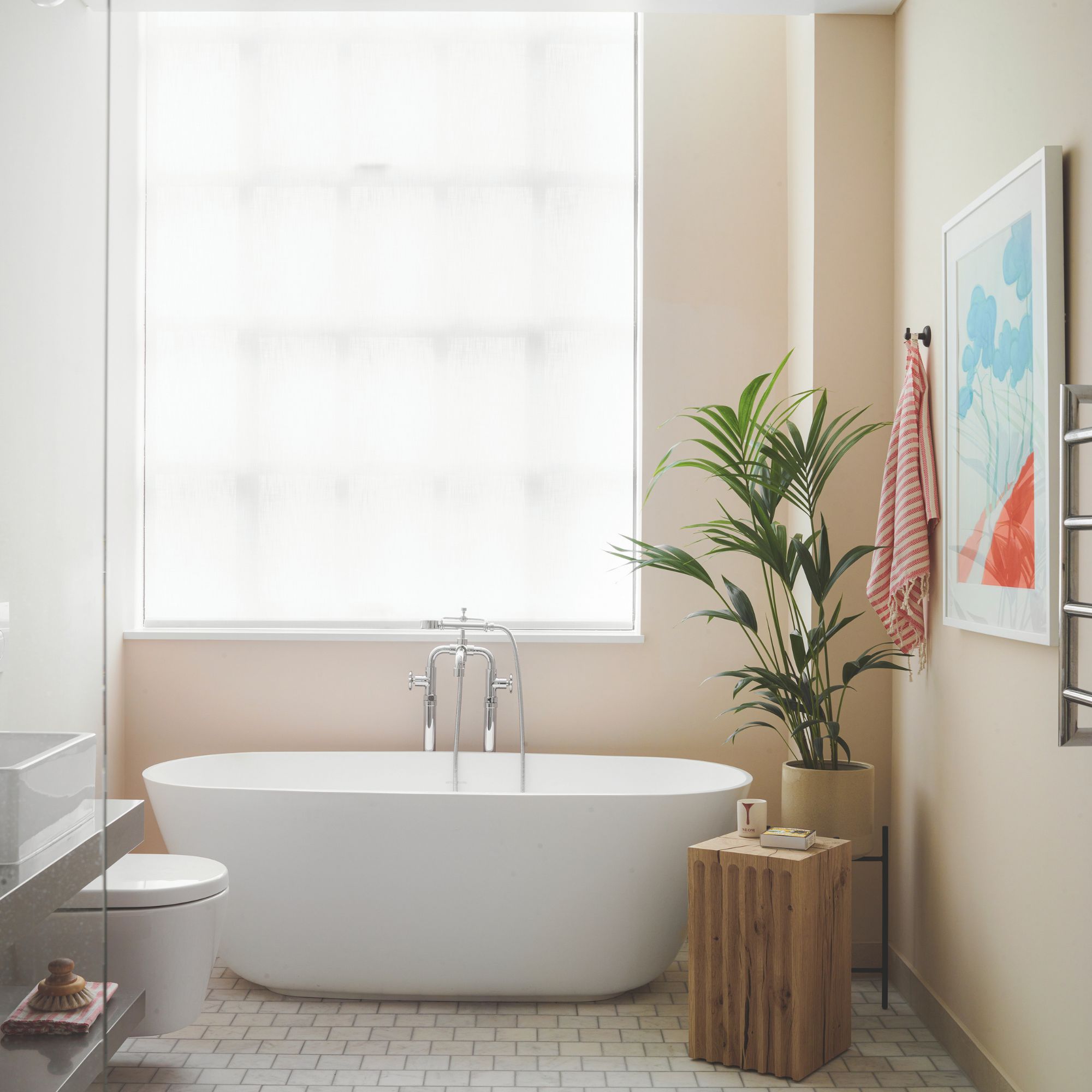 Bathroom with pink walls, deep tub and large window, wooden side table and colourful artwork