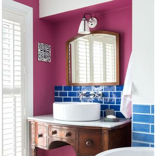 a wooden washstand with an above counter white sink, with a blue tiled wall behind it and hot pink walls