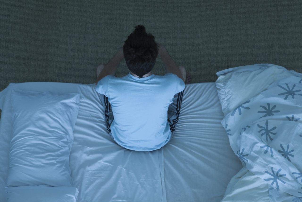 Man sits up right on the edge of a bed as he can&#039;t sleep