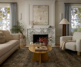 Modern living room with cream boucle armchair, printed rug, wood coffee table, blue drapes and marble fireplace