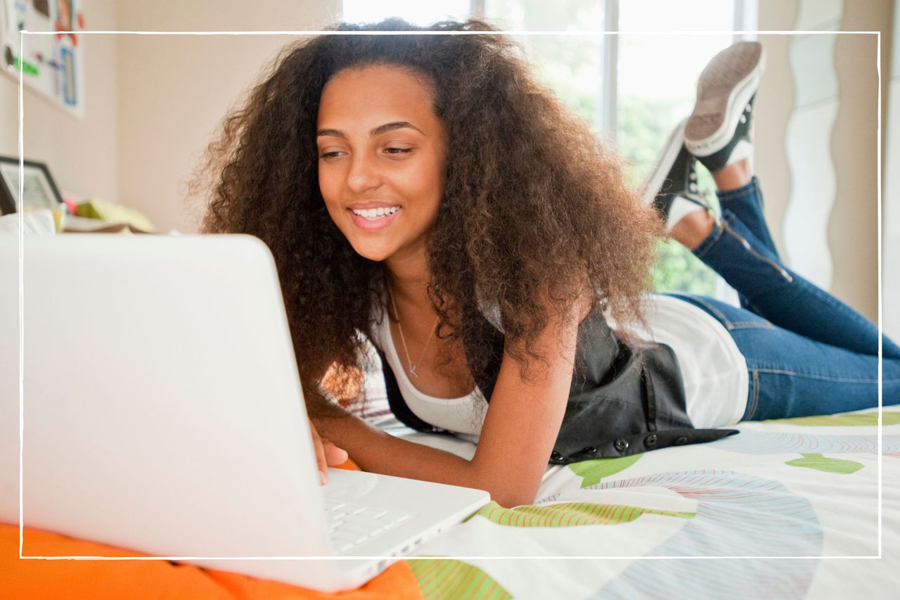 smiling teen girl lying on her bed looking at her laptop