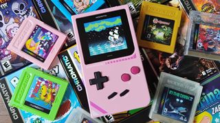 Modretro Chromatic in pink sitting on Game Boy game boxes surrounded by cartridges.