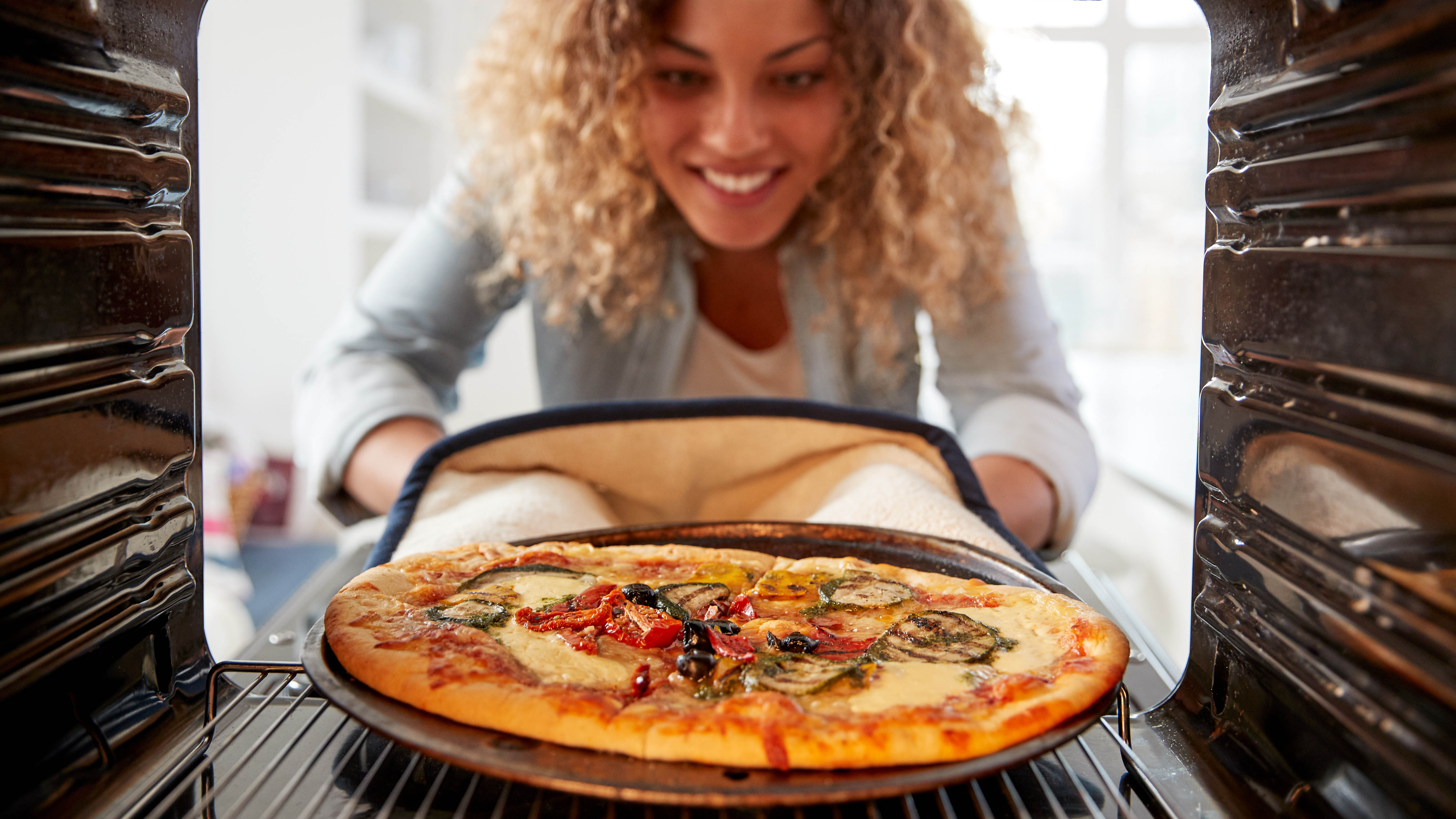 Женщина ставит пиццу в духовку в перчатках и подносе