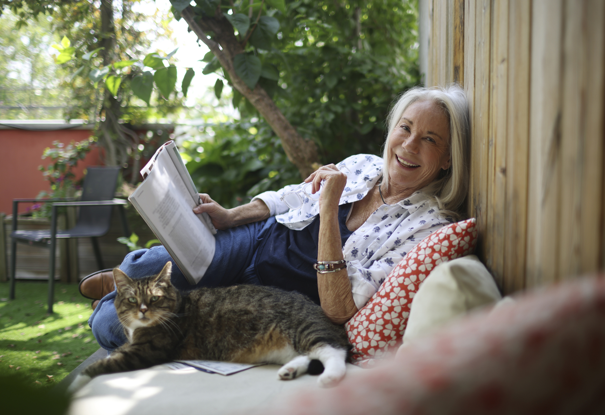 A senior woman reading a newspaper with her cat on her balcony