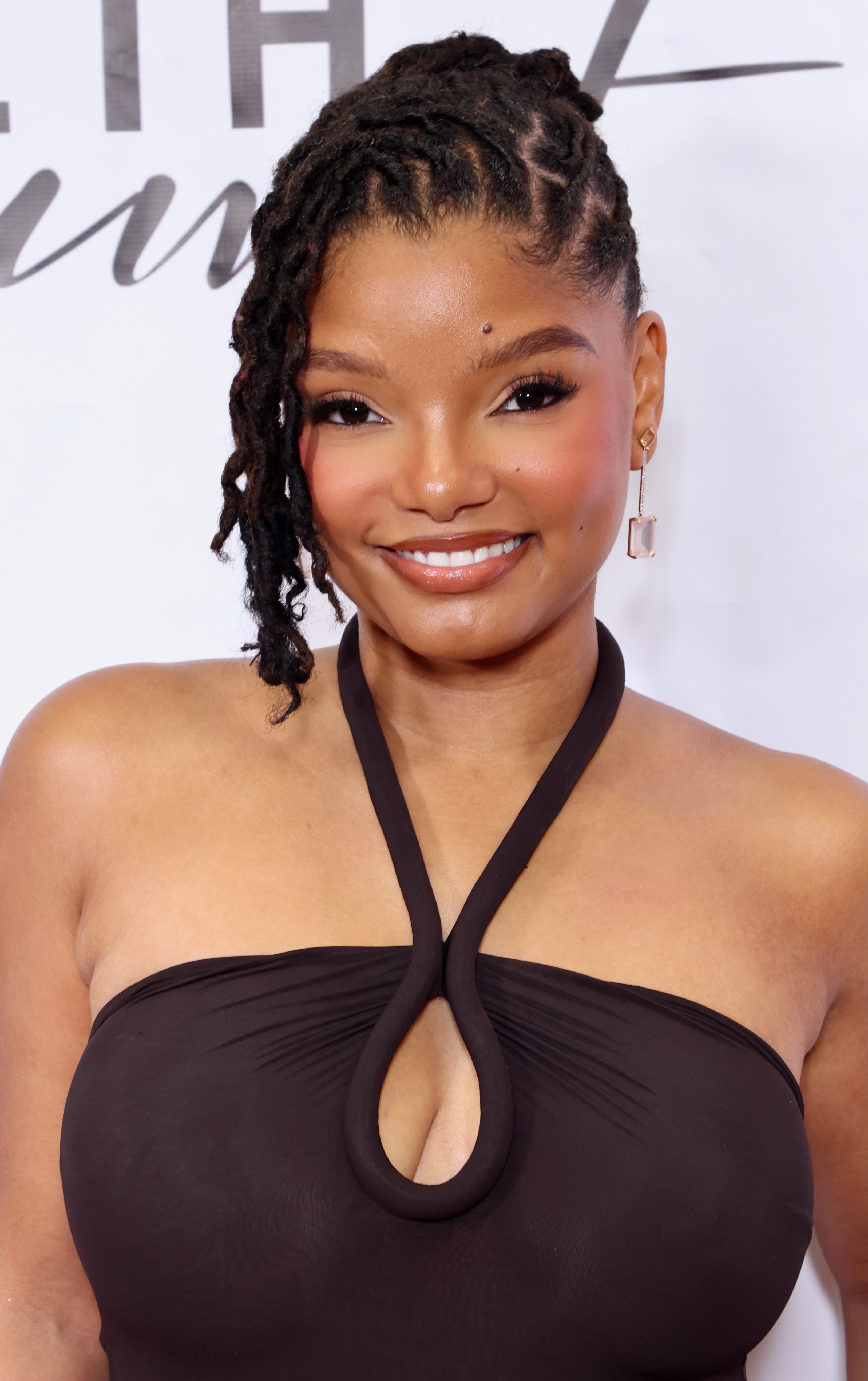 a black woman with locs wearing a brown halter top and posing in front of a white background