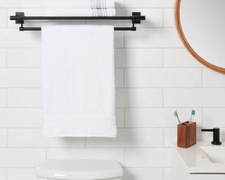 A black towel rack above a toilet in a white bathroom with a circular wooden mirror
