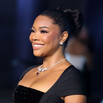 a black woman with dark hair pulled into a bun poses in front of a blue background