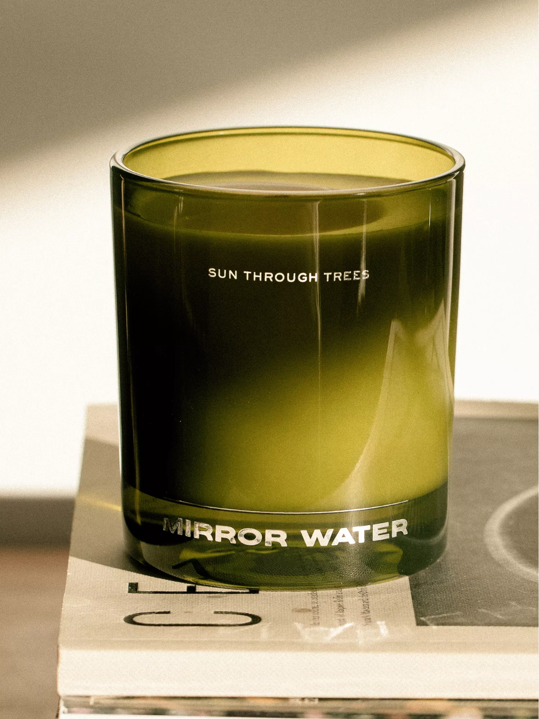 A green glass scented candle, on a book, from MIRROR WATER