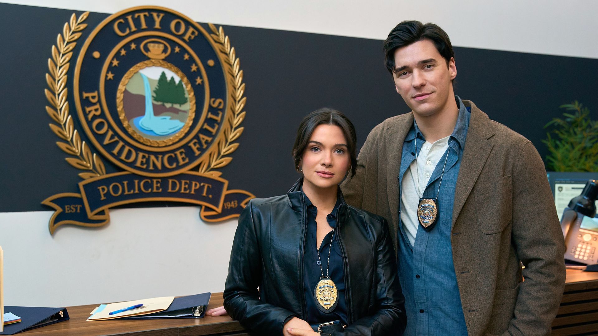 Cora and Liam stand in front of the Providence Falls police department sign