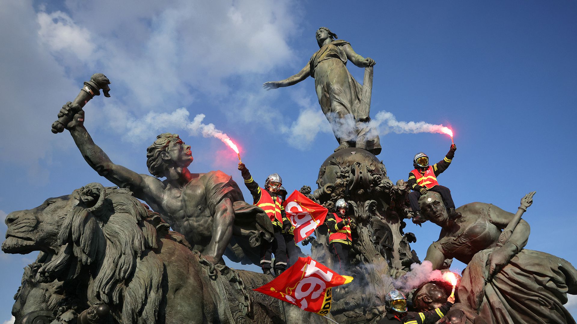 
                                Firefighters wave flares and trade union flags as they climb the 'Triumph of the Republic' statue in Place de la Nation during a public sector workers' rally in Paris, France
                            