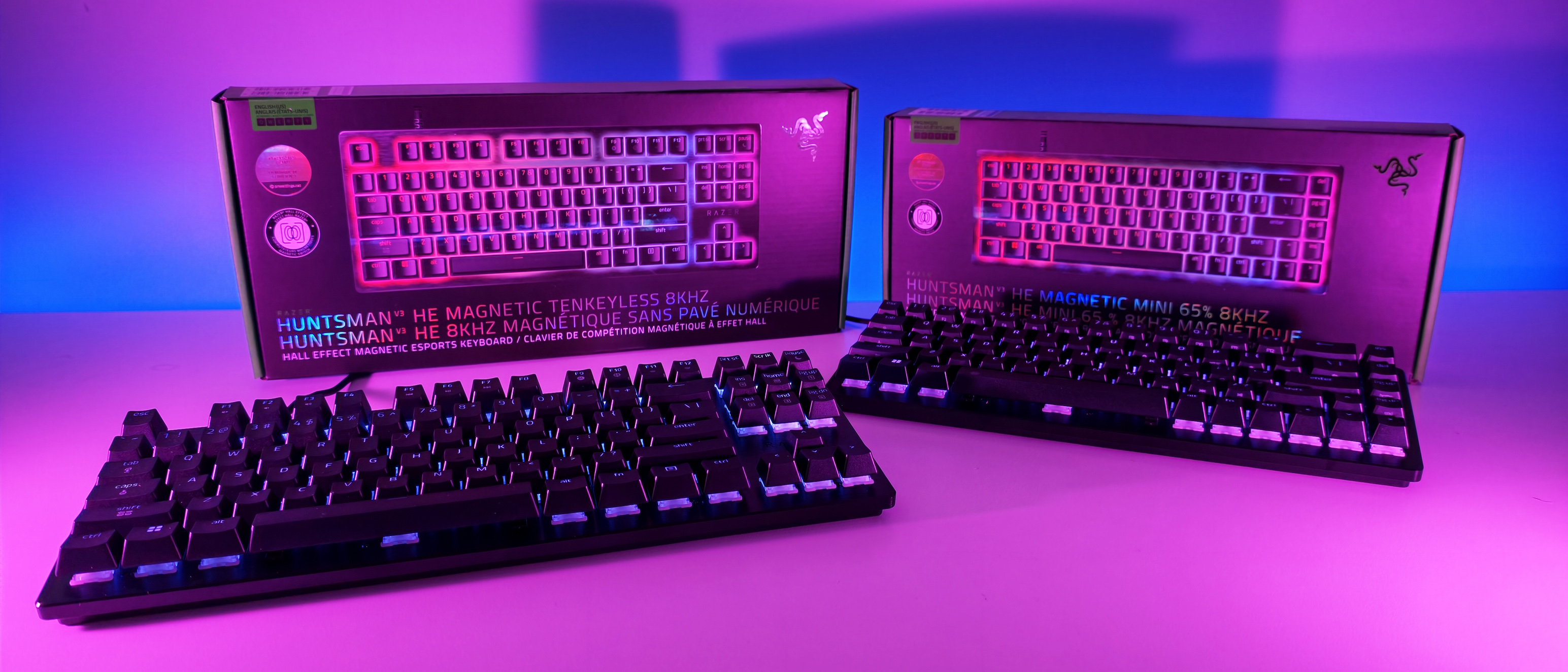 Razer Huntsman V3 HE TKL and Mini 65% gaming keyboards displayed in front of their product boxes under vibrant pink lighting.