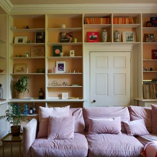 A living room with a pink velvet sofa and a built-in library along the walls wrapped around the door