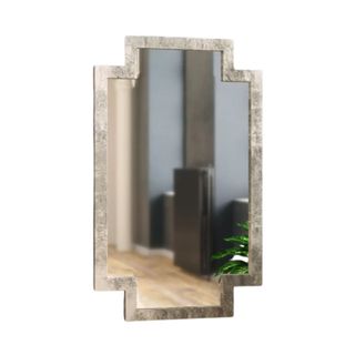 A light gold framed mirror with longer sides and a shorter top and bottom, making a geometric shape, reflecting a gray wall and light wooden floor