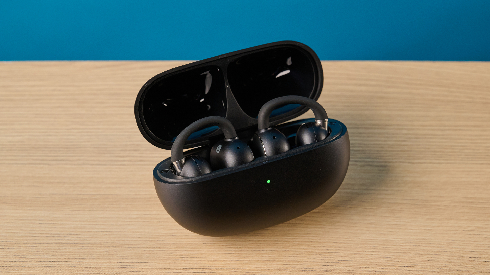 EarFun Clip 2 in black on table photographed in front of a blue background