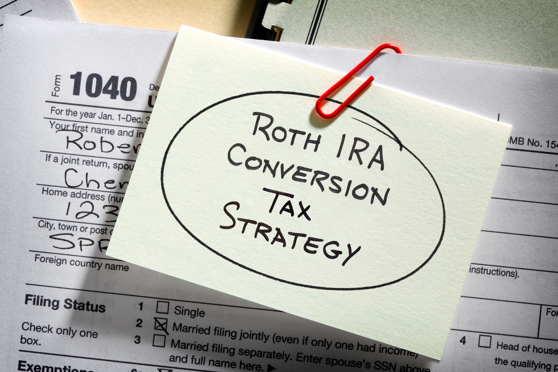 A note paperclipped to an IRS 1040 tax form with Roth IRA conversion tax strategy written on it.
