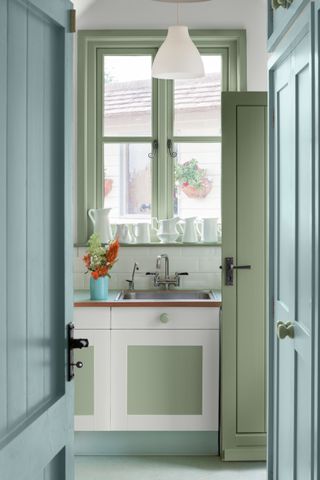 blue and green painted kitchen, vintage style, window painted to march door and inner units, vase of flowers, white ceramics on windowsill