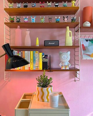 A wall shelf with books and decor on, hung up on a pink wall