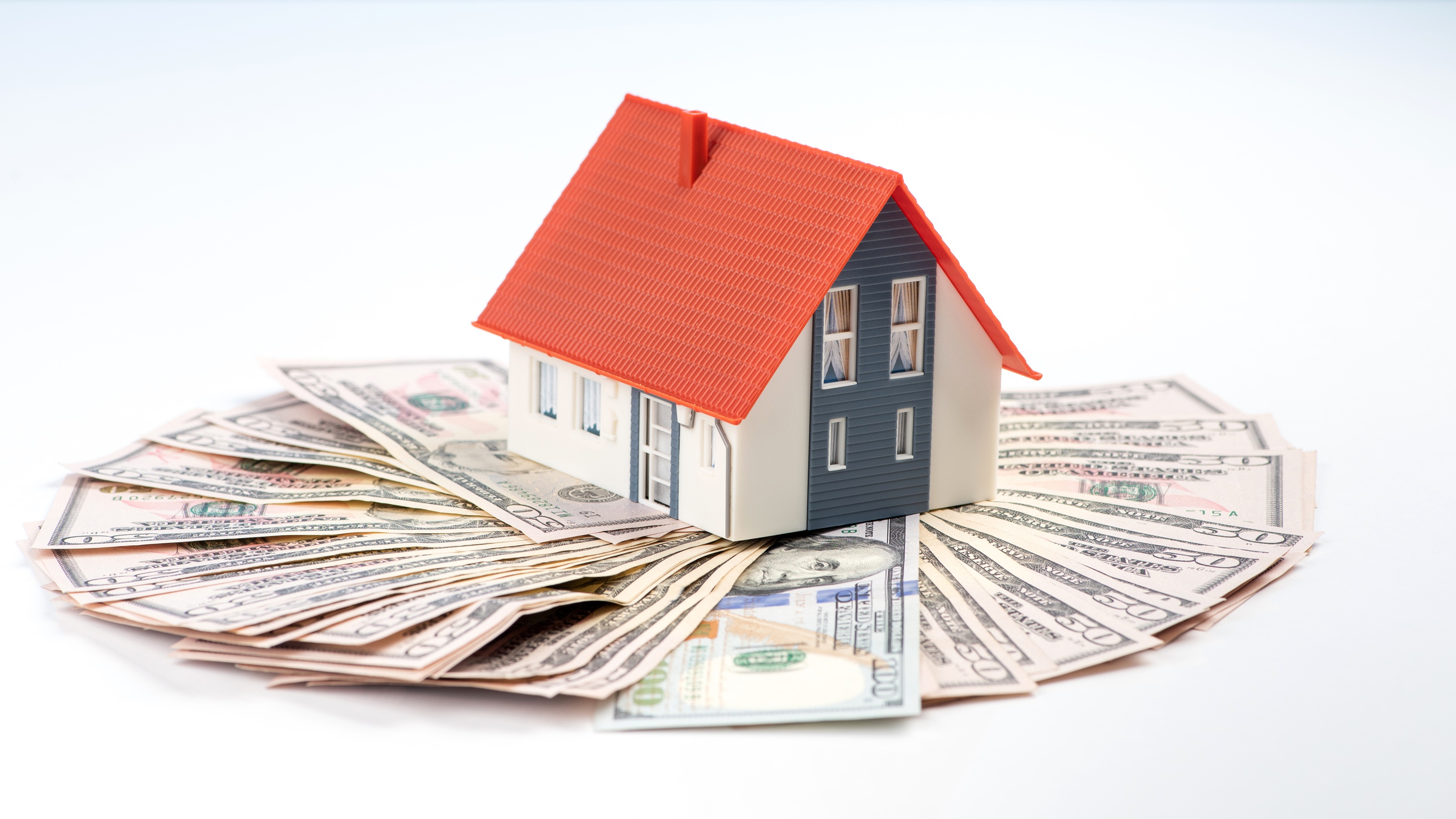 A model house atop fanned-out hundred-dollar bills.