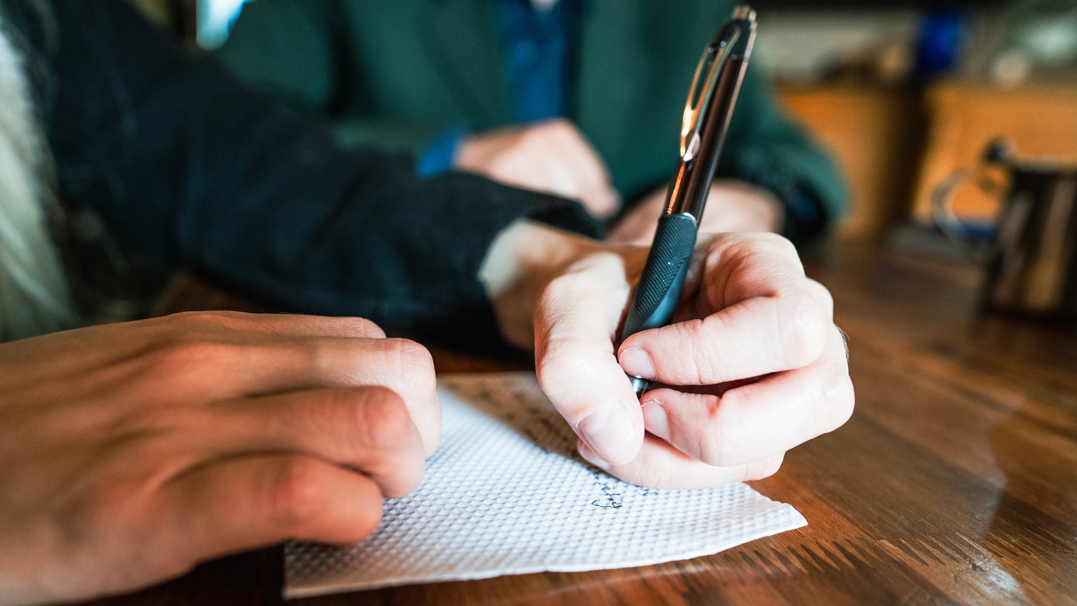 Close-up of a woman's hands writing on a napkin.