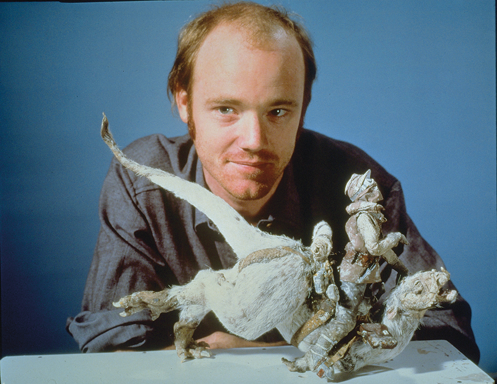 A man poses behind a miniature alien creature model and rider