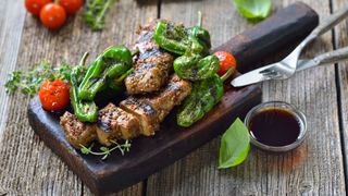 Grilled vegan seitan steaks with pimientos de padron and served with a herb soy sauce on a rustic wooden background