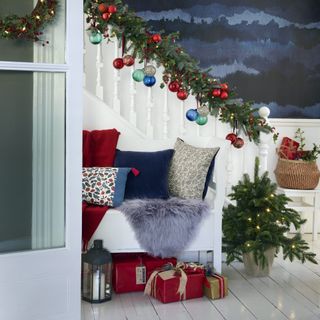 white staircase dressed for christmas with bench filled with cushions and gifts under