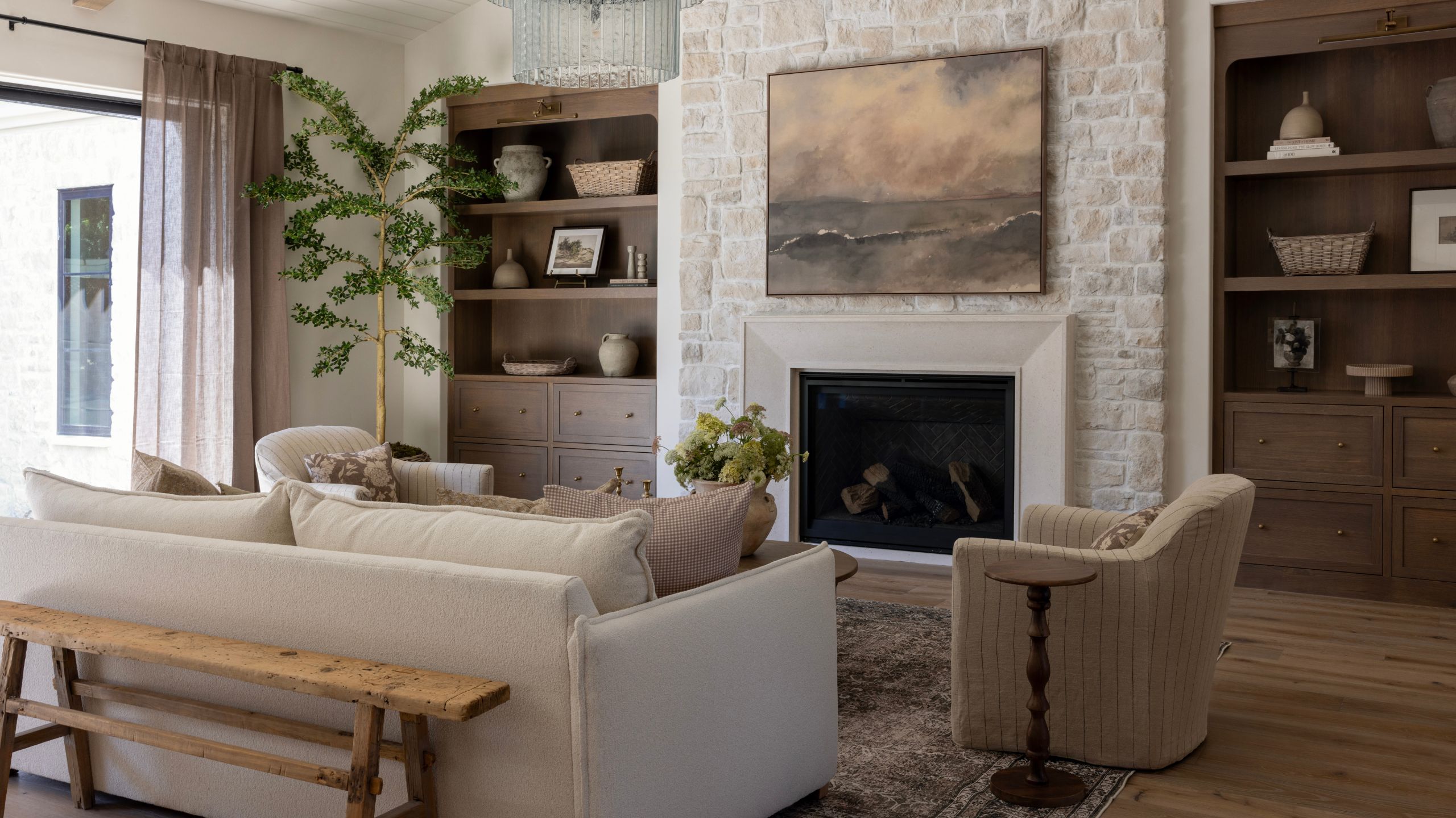 a neutral layered new build living room with stone fireplace, dark wooden alcove cabinetry, neutral linen couch and layered decor