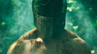 A shirtless, bloody man wearing a knight's helmet