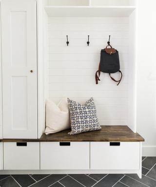 A white mudroom with a boot bench, drawers for shoes and black wall hooks