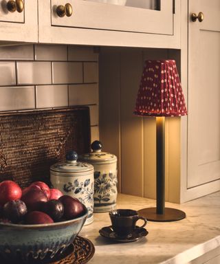 small rechargeable table light with metal base and red and white dotted pleated shade stood on kitchen worktop next to wall units