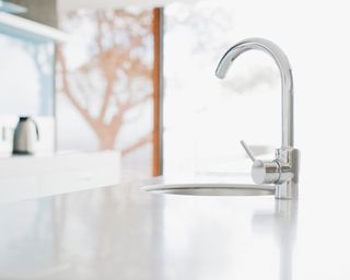 Silver kitchen faucet on white counter with light from doorway behind