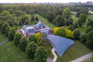 Ariel view of the Serpentine Gallery building with brick walls and a tiled roof surrounded by trees