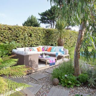 Sofa on a decked area beside a hedge, a gravelled area and lawn.