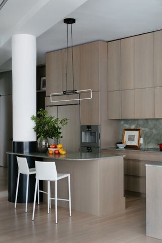 A muted brown kitchen with soft green, slim-profile countertops and curved island around a large black and white structural column