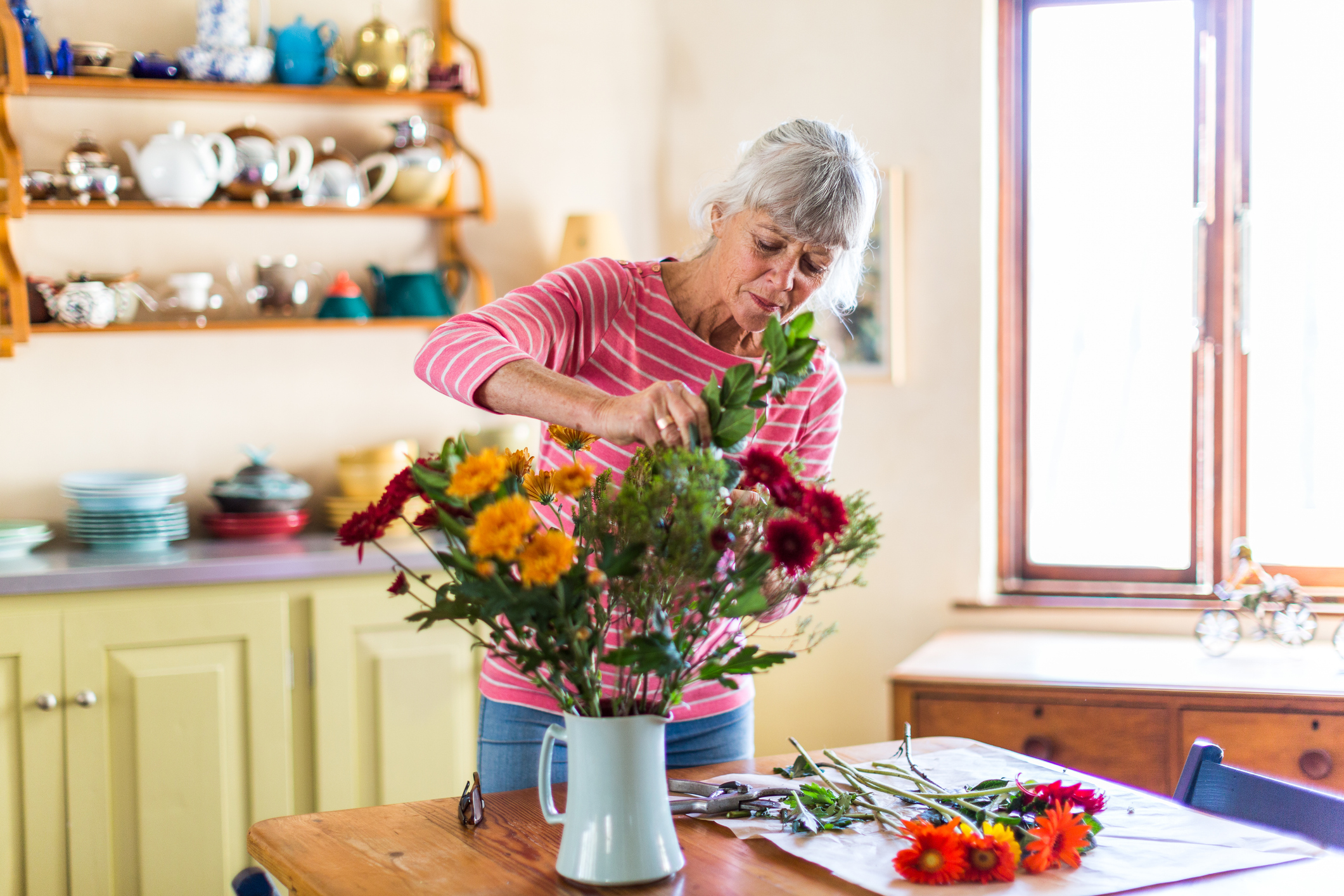 Woman arranging flowers on a kitchen table.