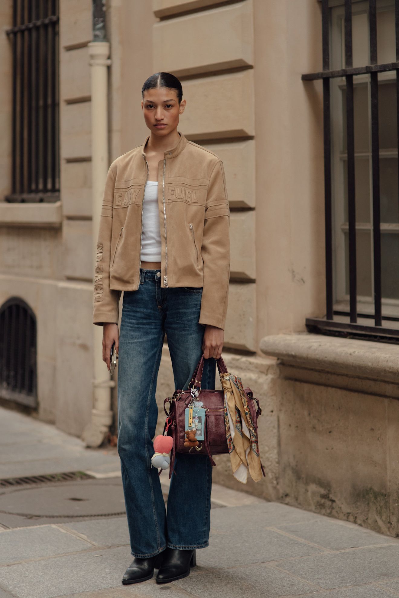 Woman in flare jeans, black heeled boots, suede jacket, white tank, and burgundy tote.