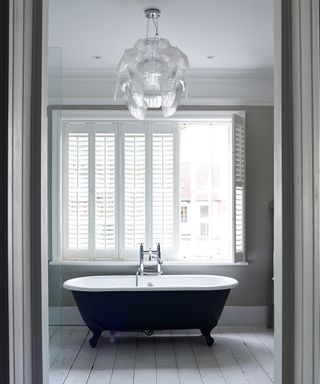 An example of bathroom lighting ideas showing a statement light in a bathroom with a black rolltop bath