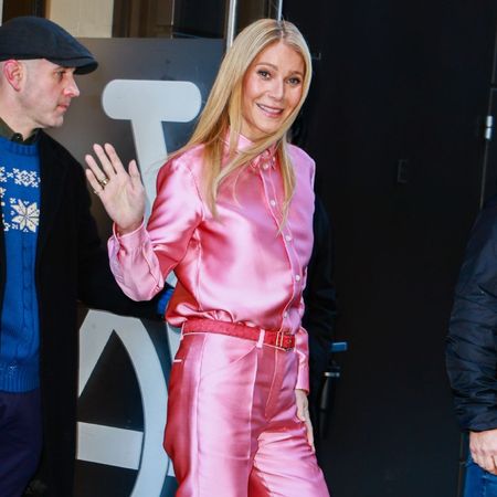 Gwyneth Paltrow steps outside wearing a pink satin trouser and shirt set with pink high vamp heels.