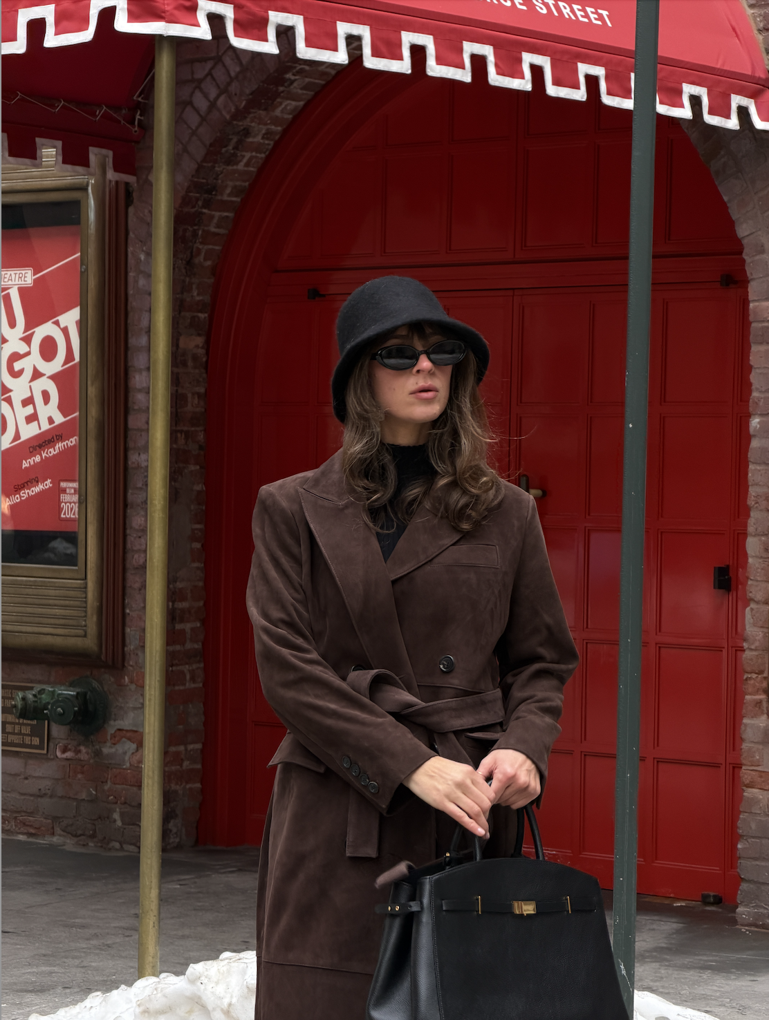 Kathryn Zahorak wearing black hat, brown coat, sunglasses, boots, black bag in new york city